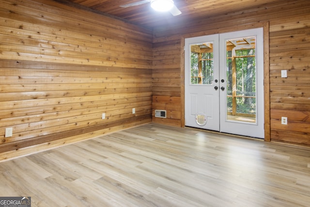 empty room with french doors, wood ceiling, ceiling fan, wooden walls, and light hardwood / wood-style flooring