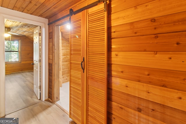 hall with a barn door, wood ceiling, vaulted ceiling, wooden walls, and light hardwood / wood-style flooring