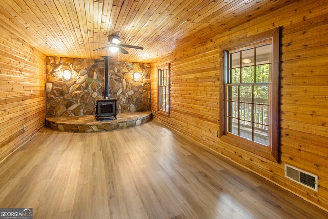 unfurnished living room featuring wood walls, wood ceiling, wood-type flooring, a wood stove, and ceiling fan