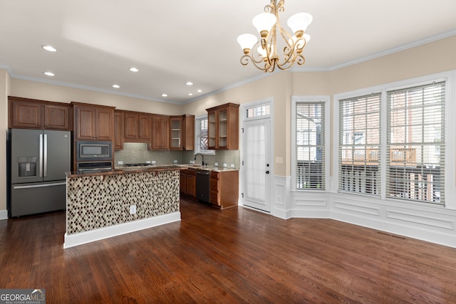 kitchen with appliances with stainless steel finishes, decorative light fixtures, dark wood-type flooring, a notable chandelier, and ornamental molding