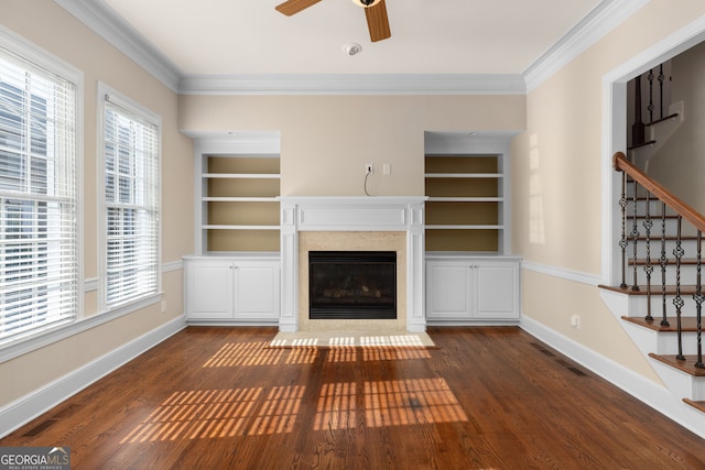 unfurnished living room featuring built in shelves, crown molding, dark wood-type flooring, and ceiling fan