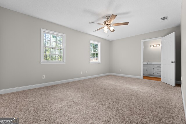 unfurnished bedroom featuring ensuite bath, carpet floors, and ceiling fan