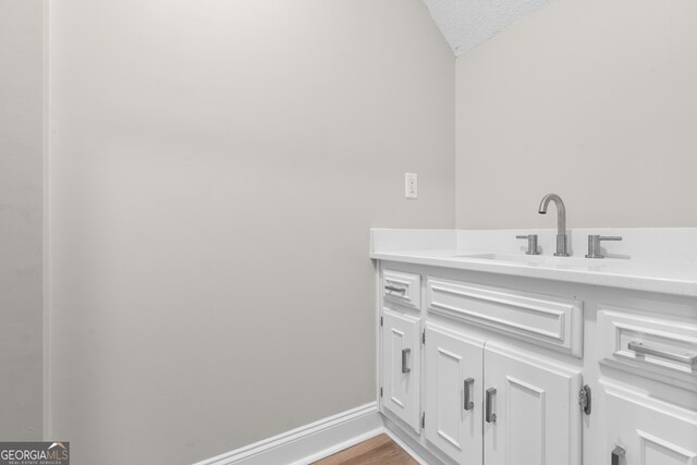 bathroom with vanity, hardwood / wood-style floors, a textured ceiling, and lofted ceiling