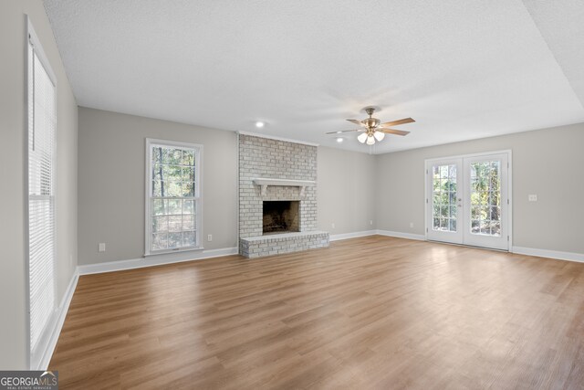 unfurnished living room with ceiling fan, a wealth of natural light, light wood-type flooring, and a brick fireplace