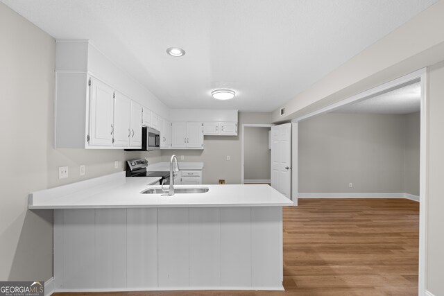 kitchen featuring sink, light wood-type flooring, kitchen peninsula, stainless steel appliances, and white cabinets