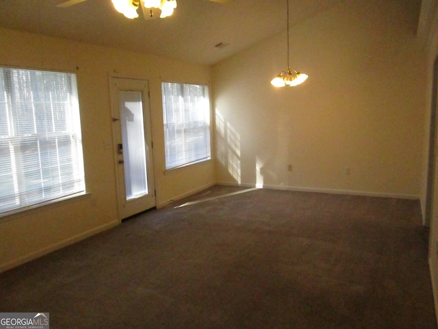 interior space featuring a wealth of natural light, vaulted ceiling, dark carpet, and ceiling fan with notable chandelier