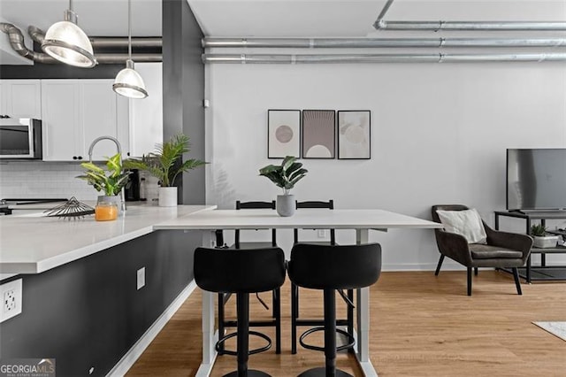 kitchen featuring a kitchen bar, hanging light fixtures, light hardwood / wood-style floors, stainless steel appliances, and decorative backsplash