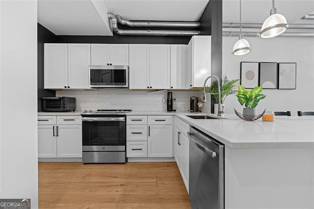 kitchen featuring sink, appliances with stainless steel finishes, pendant lighting, and white cabinets