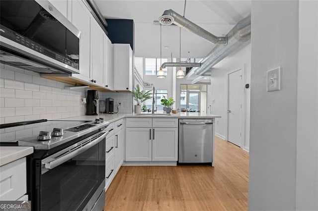 kitchen featuring tasteful backsplash, appliances with stainless steel finishes, white cabinetry, light wood-type flooring, and pendant lighting