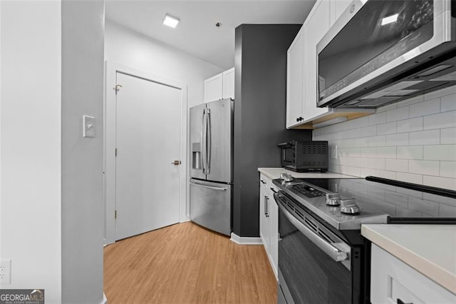 kitchen with backsplash, appliances with stainless steel finishes, light hardwood / wood-style flooring, and white cabinetry