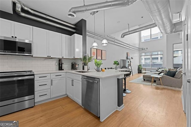 kitchen with appliances with stainless steel finishes, white cabinetry, a high ceiling, pendant lighting, and light hardwood / wood-style floors