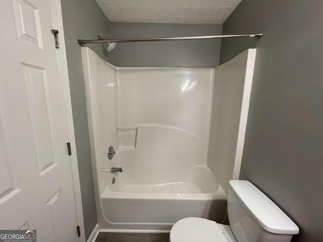 bathroom with a textured ceiling, toilet, and shower / bath combination