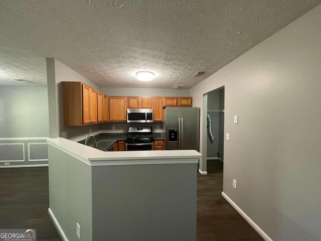 kitchen with appliances with stainless steel finishes, a textured ceiling, kitchen peninsula, and dark hardwood / wood-style floors