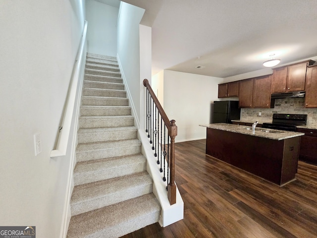 kitchen with black appliances, sink, backsplash, dark hardwood / wood-style floors, and a kitchen island with sink