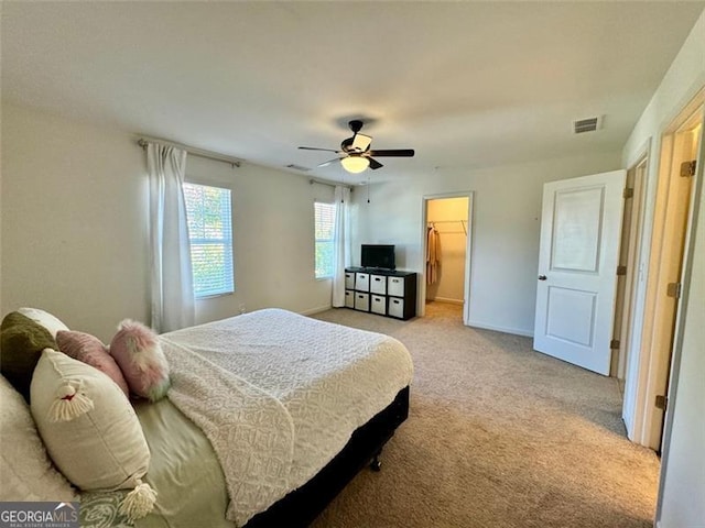 bedroom featuring a spacious closet, ceiling fan, a closet, and light carpet