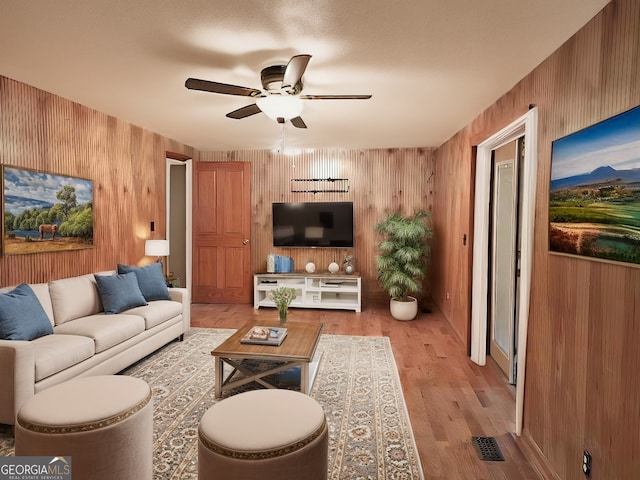 living room with wood walls, a textured ceiling, light wood-type flooring, and ceiling fan