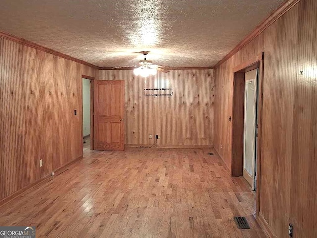 spare room with light hardwood / wood-style floors, wood walls, ornamental molding, and ceiling fan