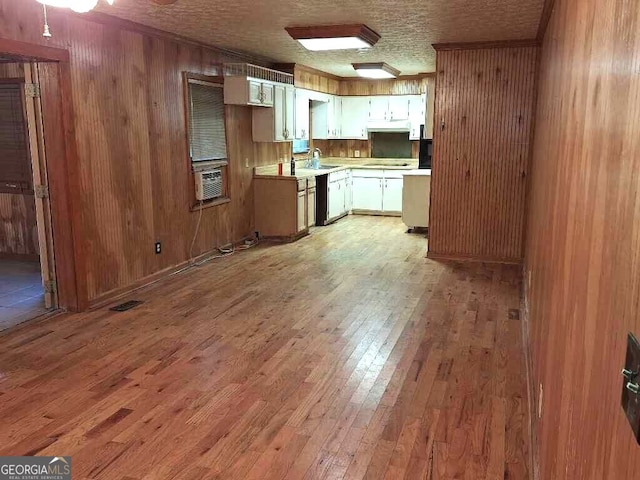 kitchen with white cabinets, a textured ceiling, light hardwood / wood-style flooring, dishwasher, and wood walls