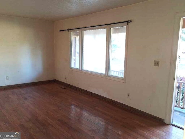 empty room with a textured ceiling and dark hardwood / wood-style flooring