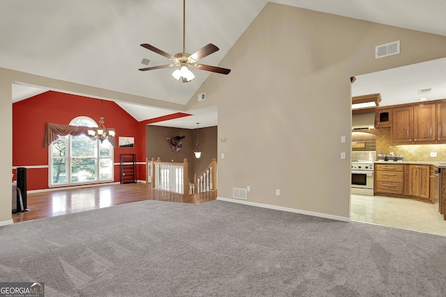 unfurnished living room featuring ceiling fan with notable chandelier, light colored carpet, and high vaulted ceiling