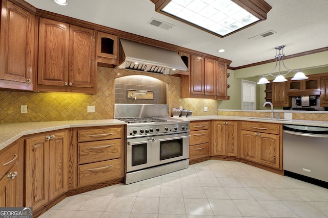 kitchen with decorative backsplash, wall chimney range hood, sink, decorative light fixtures, and appliances with stainless steel finishes