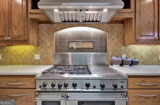 kitchen with decorative backsplash, light stone countertops, stainless steel range oven, and range hood