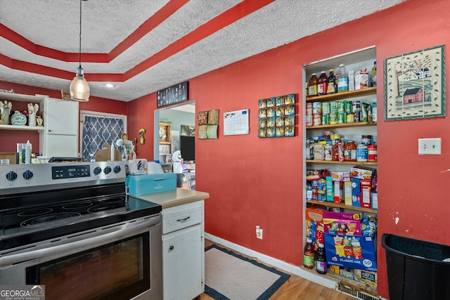 kitchen with stainless steel range with electric stovetop, a textured ceiling, hanging light fixtures, white cabinets, and light hardwood / wood-style flooring