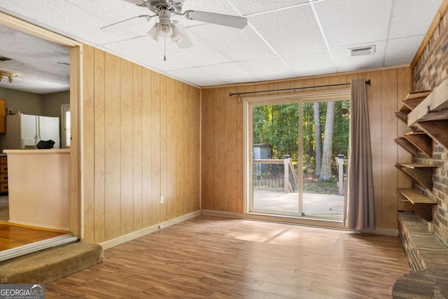 interior space with wooden walls, a drop ceiling, wood-type flooring, and ceiling fan