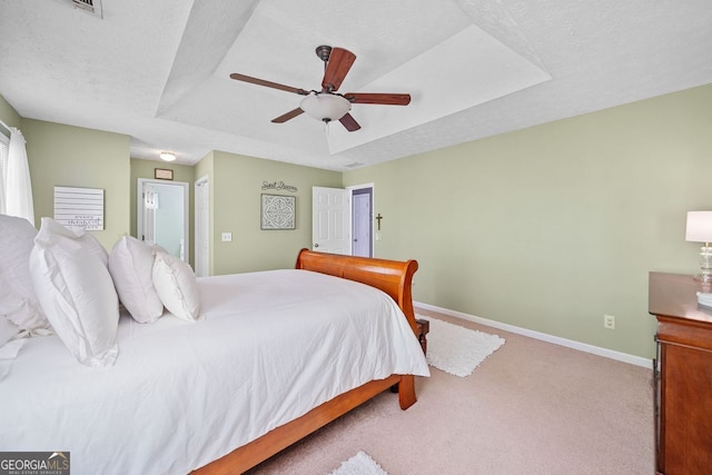 carpeted bedroom with a textured ceiling, a tray ceiling, and ceiling fan