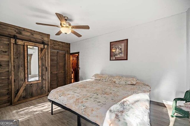 bedroom with a closet, hardwood / wood-style floors, a barn door, ceiling fan, and wood walls