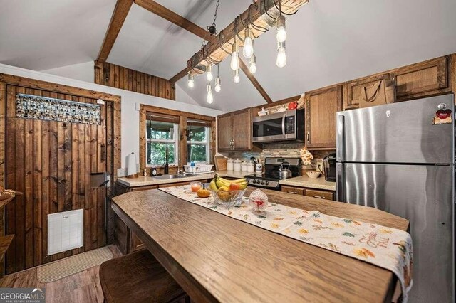 kitchen with wooden walls, stainless steel appliances, wood-type flooring, lofted ceiling with beams, and tasteful backsplash