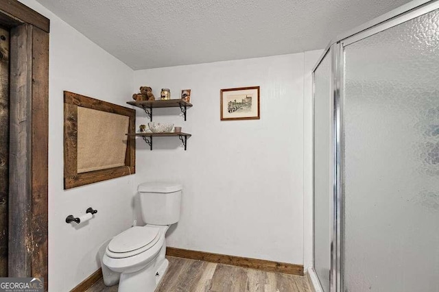 bathroom with toilet, a textured ceiling, wood-type flooring, and a shower with door