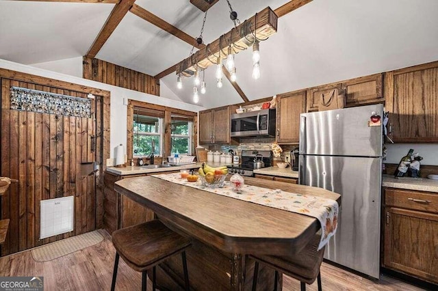 kitchen with appliances with stainless steel finishes, lofted ceiling with beams, sink, and light wood-type flooring