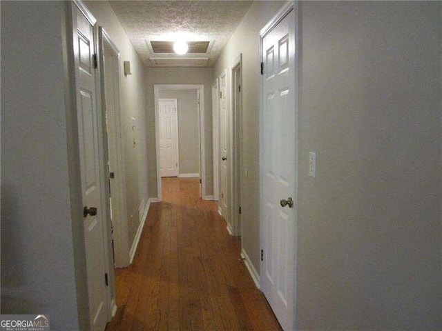 corridor with a textured ceiling and dark hardwood / wood-style floors