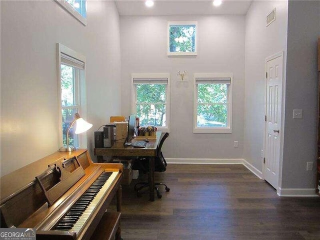 home office featuring a towering ceiling, plenty of natural light, and dark hardwood / wood-style flooring