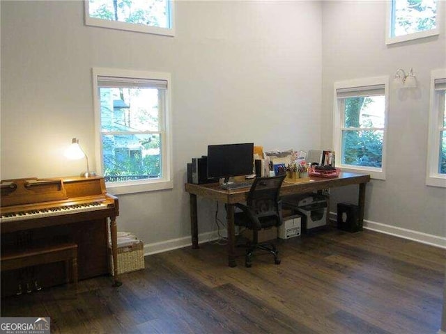 office with a healthy amount of sunlight, dark hardwood / wood-style flooring, and a high ceiling