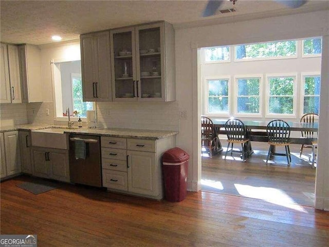 kitchen with light stone counters, backsplash, dark hardwood / wood-style flooring, stainless steel dishwasher, and sink