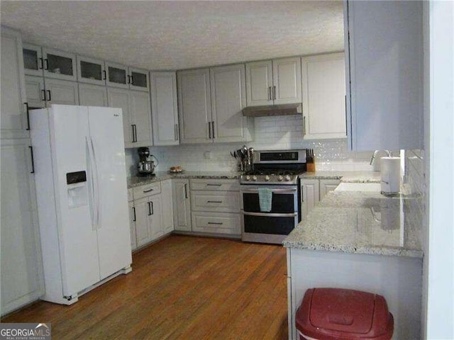 kitchen featuring white fridge with ice dispenser, sink, range with two ovens, dark wood-type flooring, and light stone counters