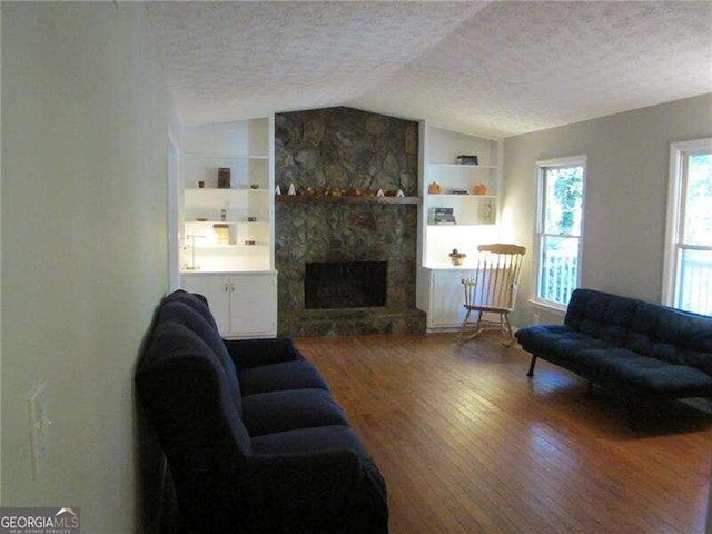 living room featuring lofted ceiling, a textured ceiling, wood-type flooring, a fireplace, and built in shelves