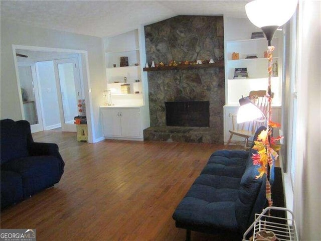 living room with lofted ceiling, a textured ceiling, hardwood / wood-style flooring, a fireplace, and built in shelves