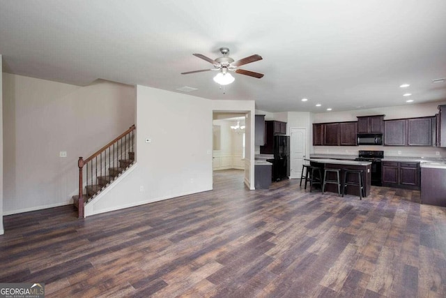 kitchen with dark brown cabinets, a kitchen island, a breakfast bar, black appliances, and dark wood-type flooring