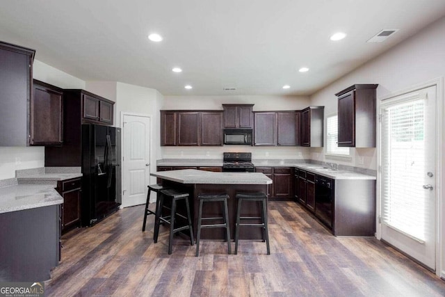 kitchen with black appliances, a kitchen bar, a kitchen island, dark brown cabinets, and dark wood-type flooring