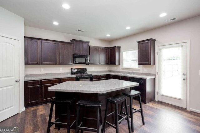 kitchen featuring black appliances, a center island, a kitchen bar, and dark hardwood / wood-style flooring