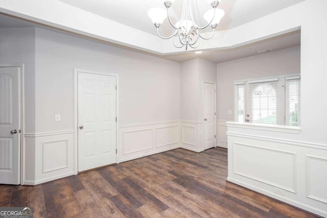 unfurnished dining area with dark hardwood / wood-style floors, a chandelier, and a tray ceiling