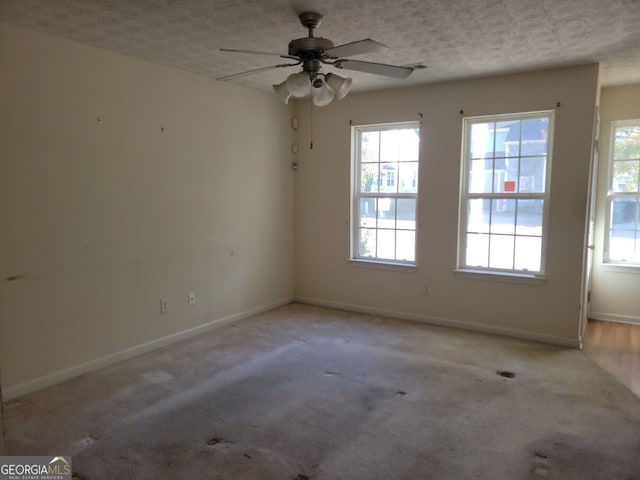 carpeted empty room featuring a wealth of natural light, a textured ceiling, and ceiling fan