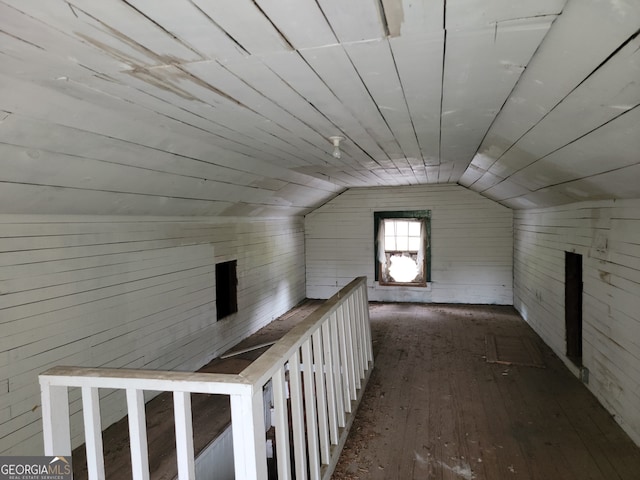 additional living space with dark wood-type flooring, vaulted ceiling, and wooden walls