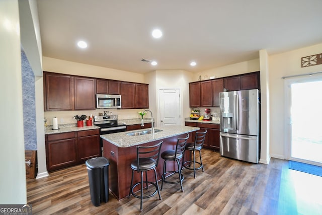 kitchen with sink, an island with sink, dark hardwood / wood-style floors, and appliances with stainless steel finishes