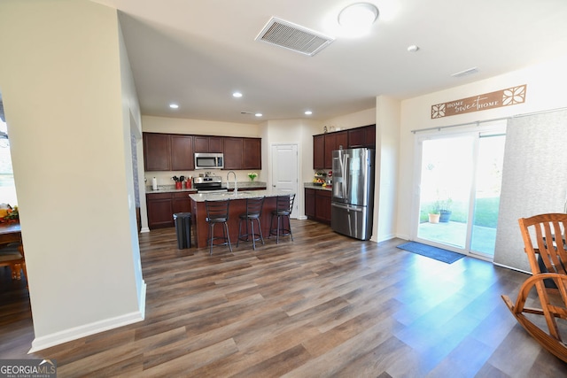 kitchen with dark hardwood / wood-style flooring, stainless steel appliances, a kitchen island with sink, and a breakfast bar area