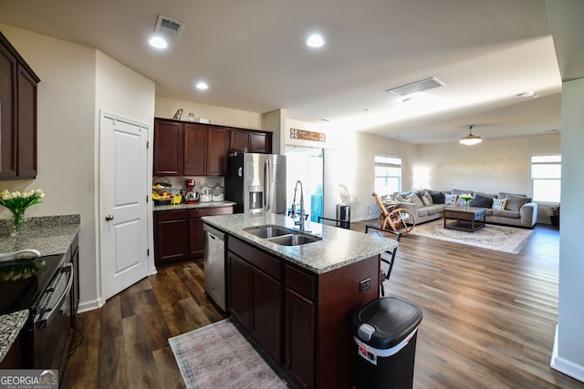 kitchen with dark brown cabinetry, stainless steel appliances, a kitchen island with sink, dark wood-type flooring, and sink