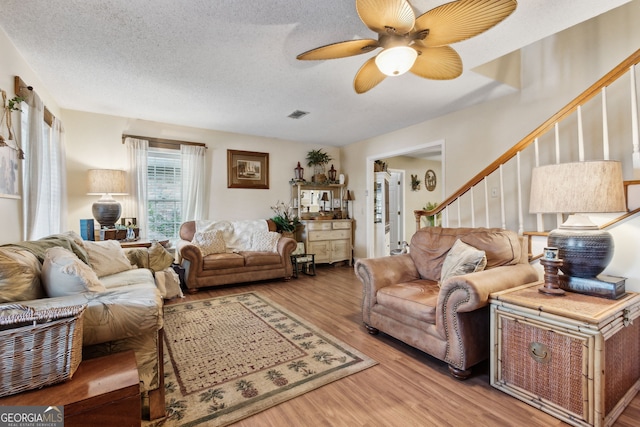 living room with ceiling fan, a textured ceiling, and light wood-type flooring